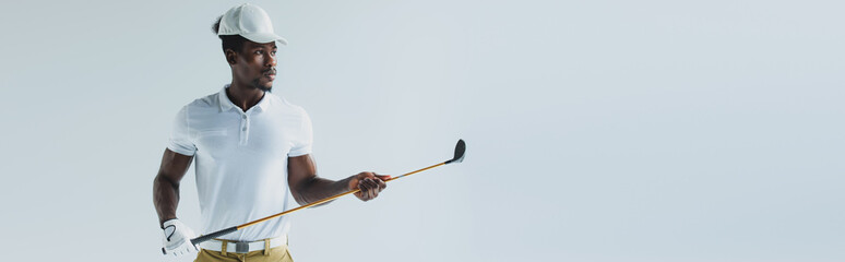 panoramic shot of handsome african american sportsman holding golf club isolated on grey