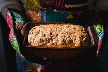 Person Holding a Loaf of African Seed Bread with Two Oven Mits
