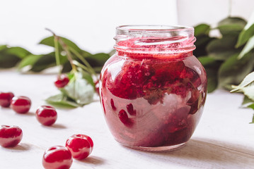 Fresh cherry jelly with fruit on a wooden background near the berries and green leaves.