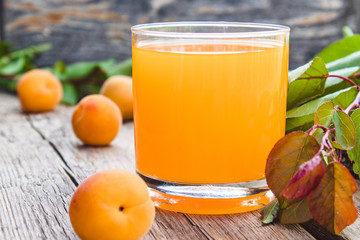 Fresh apricot juice with apricots and a branch with green leaves on the background of old boards.