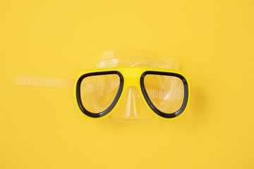 A yellow snorkel and diving mask on a yellow background. overhead lay flat