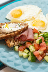 Fototapeta na wymiar Close up of hotel breakfast with fried eggs, toasts with ham and cheese and summer salad