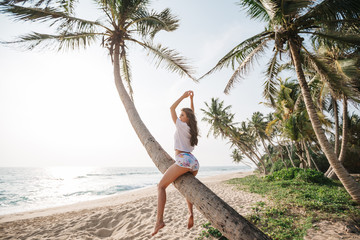 Woman sit on a palm tree at tropical beach against ocean. Vacation concept. Happy young woman relax...