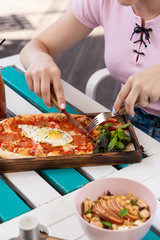 Woman is eating rome pizza with pepperoni, tomatoes and fried egg on a summer terrace