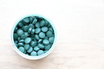 Fototapeta na wymiar Spirulina and Chlorella tablets in a bottle on a white wooden table. Nutrition supplements for health, top view