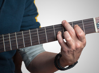 Man playing on classic guitar against silver background. Handsome young men playing guitar