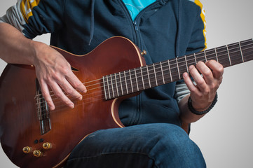 Obraz premium Man playing on classic guitar against silver background. Handsome young men playing guitar