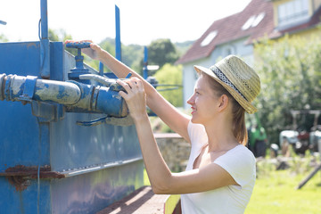 Fototapeta premium Junge Frau im Garten öffnet Wasserhahn zur Bewässerung