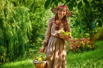 Pretty smiling teenager girl in the garden with basket with apples harvest picked from apple tree....