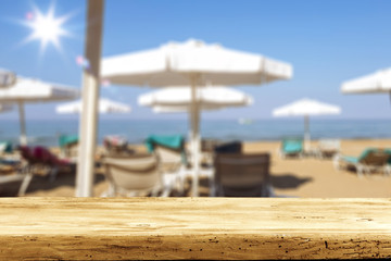 Table background with some umbrellas and sun beds with a blurred beach view.