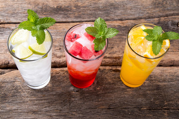 Glasses of lime, water melon, orange soda drinks on woodenbackground. 