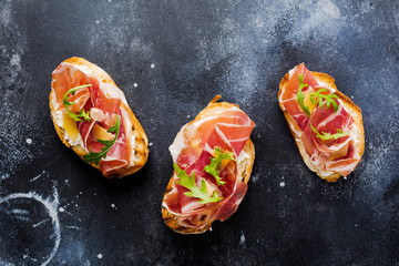 Open sandwiches with jamon, arugula and hard cheese on a concrete old dark background. Rustik style.Top view.