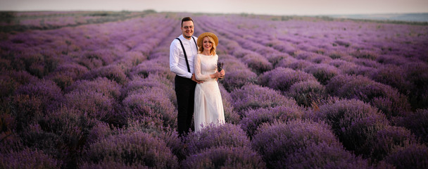 Young couple standing in middle of blooming lavender field at sunrise