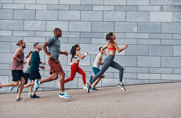 Full length of people in sports clothing jogging while exercising on the sidewalk outdoors