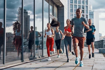 Zelfklevend Fotobehang Full length of people in sports clothing jogging while exercising on the sidewalk outdoors © gstockstudio