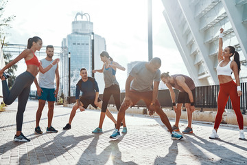 Full length of people in sports clothing warming up and stretching while exercising on the sidewalk outdoors