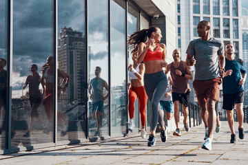 Full length of people in sports clothing jogging while exercising on the sidewalk outdoors