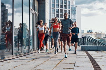 Full length of people in sports clothing jogging while exercising on the sidewalk outdoors