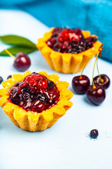 Small berry cake and ripe berries on a blue wooden background. Delicious dessert.