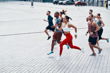 Full length of young people in sports clothing jogging while exercising on the sidewalk outdoors