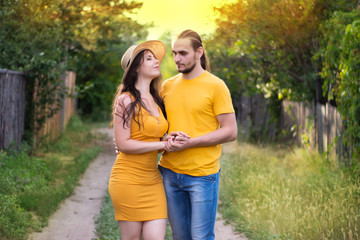 Fototapeta premium Young woman in a hat and a man walking down the street. Portrait of a couple in love. Summer mood, hot sunny day.