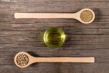 CBD oil. Glass jar with hemp oil and two wooden spoons with cannabis grains and flour on old wooden boards. 