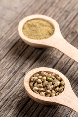 Two wooden spoons with cannabis grains and flour on  diagonal old wooden boards. 