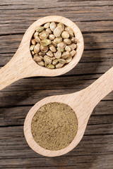 Two wooden spoons with cannabis seeds and hemp flour on old cracked wooden board.