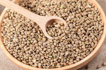 Close-up hemp grains in big round wooden plate with wooden spoon on burlap. 