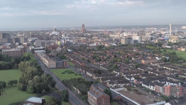Aerial cityscape across Liverpool city buildings, cathedral, radio city tower along skyline. Lowering pull back.