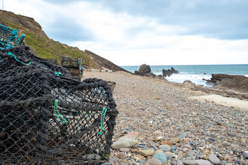Lobster nets on a pebble beach with waves and the sea in the background.