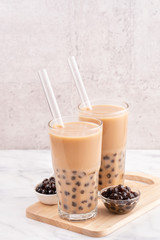 Tapioca pearl ball bubble milk tea, popular Taiwan drink, in drinking glass with straw on marble white table and wooden tray, close up, copy space.