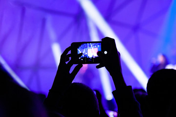 Fototapeta na wymiar Raised hand of a man with a smartphone in front of bright lights record a concert.