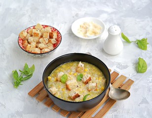 Summer soup of sweet corn and potatoes in a black bowl on a light gray concrete background. Served with croutons and grated parmesan cheese. Italian food. Selective focus.