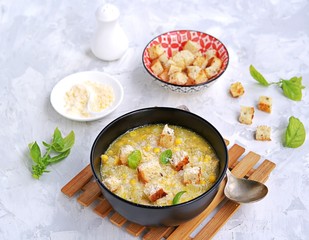 Summer soup of sweet corn and potatoes in a black bowl on a light gray concrete background. Served with croutons and grated parmesan cheese. Italian food. Selective focus.