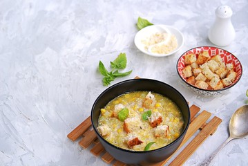 Summer soup of sweet corn and potatoes in a black bowl on a light gray concrete background. Served with croutons and grated parmesan cheese. Italian food. Selective focus.
