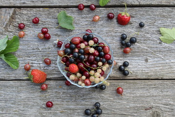 Fresh berries of white, black, currant, cherry, gooseberry and strawberry are on the plate and scattered around it.