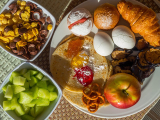 breakfast served with croissant, eggs, melon, flakes with milk, apple fruit, pancakes, mix of jams, eggplant slices. Balanced diet