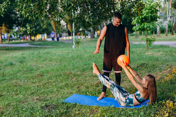 Man trainer teaching a woman do exercise with a ball