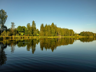 beautiful summer landscape with calm lake, reflections of different trees, blue sky, calm water, Latvia