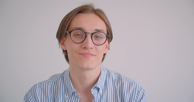Closeup portrait of young attractive caucasian businessman in glasses looking at camera smiling happily indoors in a white apartment
