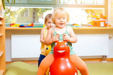 Little girls riding on play horses in kindergarten
