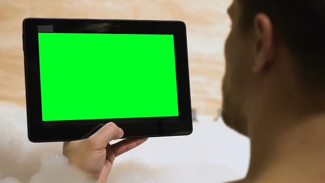 Male holding prekeyed tablet, lying in bathtub, template for advertisement, app