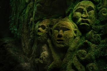 Fototapeta na wymiar Carving demons faces on wall background covered with moss texture in Bali