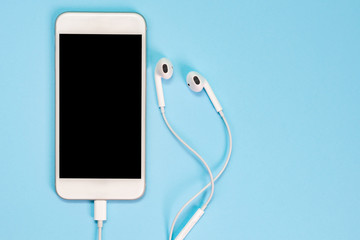 White smartphone on the blue background with headphones. View from above.
