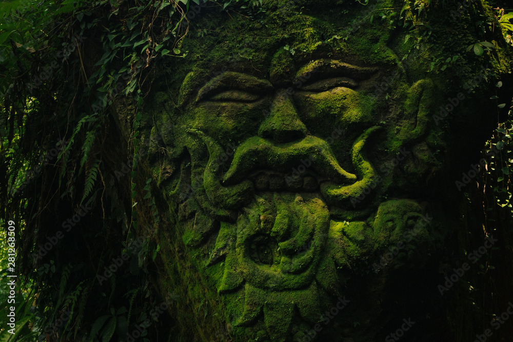 Wall mural carving demons faces on wall background covered with moss texture in bali