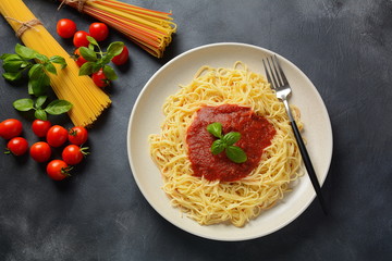 Classic Italian spaghetti pasta with tomato sauce and basil on plate on dark table