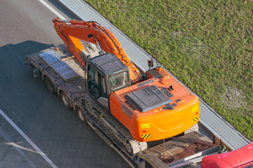 Truck with a long trailer platform for transporting heavy machinery, loaded excavator. Highway transportation.