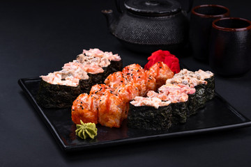 Close up of sashimi sushi set with chopsticks and soy on black background. Korea rolls and green tea cups and teapot, copy space. Japanese food.