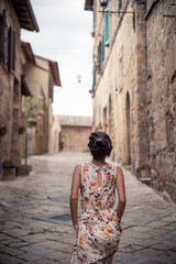 Fototapeta na wymiar Young asian girl walking in Monticchiello town on summer day. Amazing promenade with traditional old stone houses - Tuscany, Italy, Europe